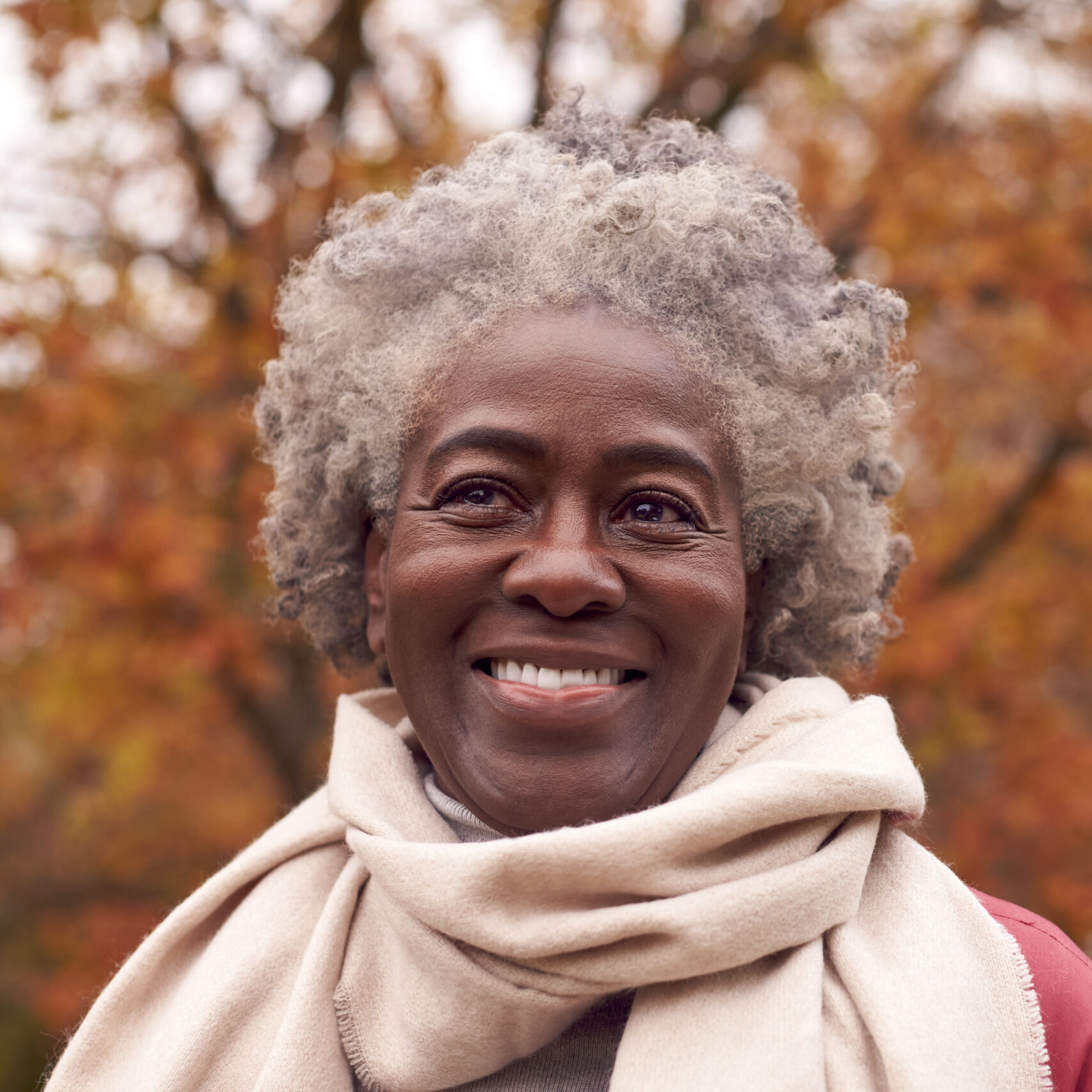 Head And Shoulders Portrait Of Senior Woman On Walk Through Autumn Countryside Against Golden Leaves