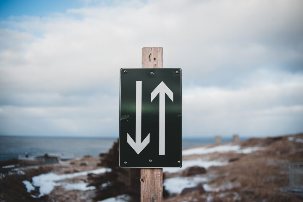 pexels-photo-7205475-7205475 Sign of two way trail on sandy shore of calm sea with snow under cloudy sky on winter day
